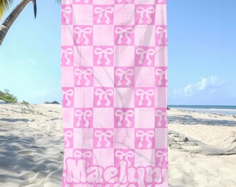 May include: Pink beach towel with a checkered pattern and pink bows. The towel has the name "Maelyn" printed on it.