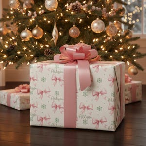 A wrapped gift with pink ribbon sits in front of a Christmas tree and another smaller wrapped box.