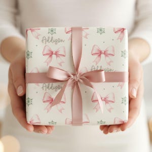 Close-up of a person holding a vertically oriented gift wrapped in pink bow and green snowflake paper with a wide satin ribbon bow.