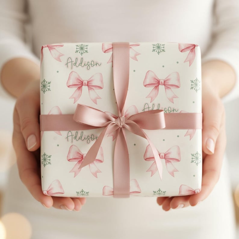 Close-up of a person holding a vertically oriented gift wrapped in pink bow and green snowflake paper with a wide satin ribbon bow.