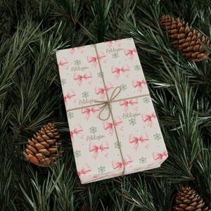 Pinecones and evergreen branches frame gift-wrapped packages decorated with pink bows.
