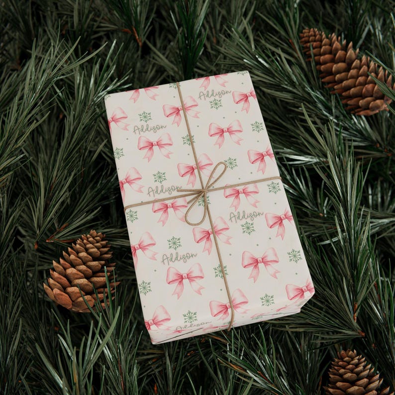 Pinecones and evergreen branches frame gift-wrapped packages decorated with pink bows.