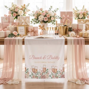 Pu&ograve; includere: Un'impostazione del tavolo per un addio al nubilato con regali, fiori e champagne. Il tavolo &egrave; decorato con una tovaglia bianca e un runner con la scritta "Brunch & Bubbly". La scena comprende calici di champagne, un libro degli ospiti e una cornice dorata.