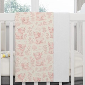 May include: A baby blanket with a repeating pattern of pink Highland cows and floral details on a cream backdrop. The blanket is folded over a white cot rail, displaying the soft, pastel design. The blanket is made of a soft material.