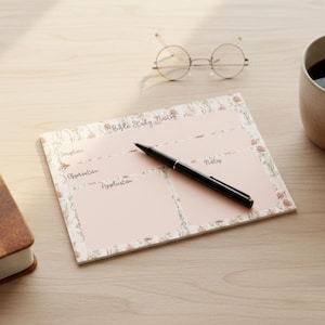 May include: A floral-bordered Bible study notes pad with a black pen, round glasses, and a mug of coffee on a light wood surface. The pad has sections for Scripture, Observation, Application, and Notes.
