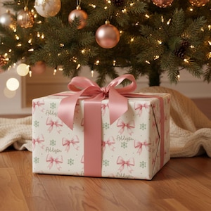 A wrapped gift with a pink bow sits on a wooden floor in front of a decorated Christmas tree.