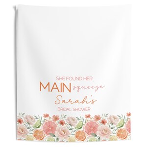 May include: White bridal shower towel with a floral border featuring pink grapefruit slices, orange slices, and green limes. The towel has the text "SHE FOUND HER MAIN squeeze Sarah's BRIDAL SHOWER" in orange and pink.