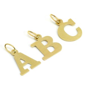 May include: Three gold-colored letter charms: A, B, and C. Each charm has a small loop at the top for attaching to a chain or bracelet. The letters are in a simple, sans-serif font and are set against a white background.