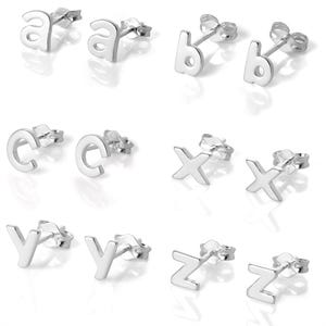 May include: A selection of silver stud earrings, each in the shape of a letter. The letters 'a', 'b', 'c', 'x', 'y', and 'z' are shown. The earrings are presented on a white background.