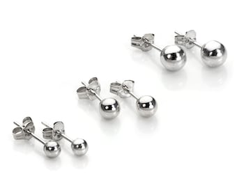 May include: Several pairs of small, silver ball stud earrings are displayed against a white background. The earrings have a simple, classic design, with a round ball at the end of a post. The earrings are likely made of a shiny metal.