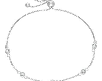 Puede incluir: Un brazalete tipo bolo plateado con una fina cadena y seis piedras preciosas redondas y transparentes. El brazalete tiene un cierre de cuentas deslizantes para ajustar la talla. El diseño es sencillo y elegante.