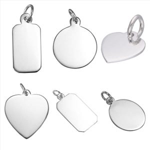 Puede incluir: Una colección de seis dijes de metal en tono plateado pulido con diversas formas, incluyendo diseños rectangulares, circulares y en forma de corazón. Cada dije cuenta con una pequeña argolla circular en la parte superior para colgar.