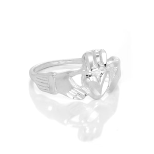 May include: A silver Claddagh ring, a traditional Irish design. The ring features a heart held by two hands, with a crown above the heart. The ring is highly polished and reflects light, set against a white background.
