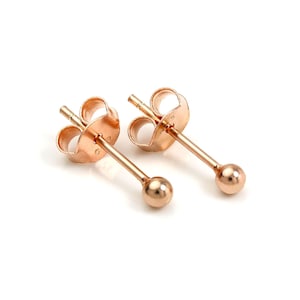 May include: A pair of rose gold ball stud earrings. Each earring features a small, round ball at the end of a straight post, with a butterfly backing. The earrings are displayed against a white background.
