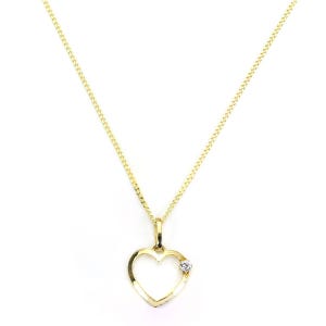 Könnte beinhalten: Goldfarbene Halskette mit herzförmigem Anhänger. Der Anhänger hat einen kleinen, klaren Edelstein auf der rechten Seite. Die Kette ist filigran. Der Hintergrund ist weiß.