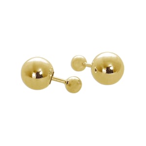 May include: A pair of gold-colored ball stud earrings. Each earring features a small ball connected to a larger ball with a short post. The earrings are set against a white background.
