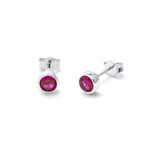 May include: A pair of silver stud earrings featuring round, bright pink gemstones. The gemstones are set in a bezel setting, and the earrings have a simple, elegant design. The earrings are displayed against a white backdrop.