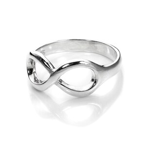May include: A polished silver ring in the form of an infinity symbol. The ring's design is a continuous loop, reflecting light. The smooth surface suggests a high-quality finish. The ring is presented on a white background, highlighting its shape and shine.