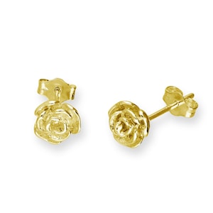 May include: A pair of gold-colored stud earrings, each shaped like a rose. The earrings are displayed on a white background, showcasing their intricate floral design and the post and backing.