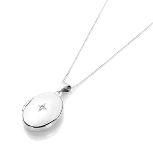 May include: A silver-colored oval locket pendant necklace. The locket has a starburst design on the front and hangs from a delicate chain. The necklace is displayed against a white background.