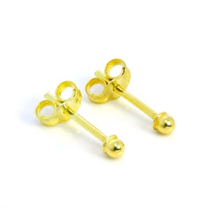 May include: A pair of small, gold-colored stud earrings. Each earring features a post with a small, round ball at the end and a butterfly backing. The earrings are set against a white background.
