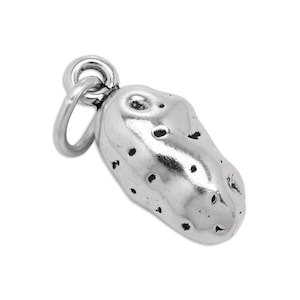 May include: A silver-toned metal charm shaped like a potato, featuring a textured surface with small, dark, recessed spots to mimic the appearance of eyes on a potato. The charm includes a small circular jump ring attached to the top end.