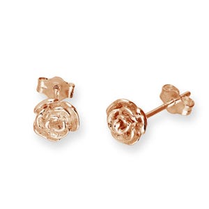 May include: Rose gold stud earrings. Each earring features a detailed rose design. The earrings are set against a white background, highlighting their delicate floral shape and metallic sheen. A classic jewelry piece.