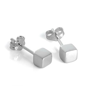 May include: A pair of silver stud earrings. Each earring has a small, square cube at the end of a post. The earrings are shown against a white background, with light reflecting off the polished metal.