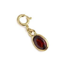 Op de afbeelding: Een gouden bedel met een dieprode ovale edelsteen gezet in een gepolijst gouden frame. De bedel is voorzien van een ronde veerringsluiting aan de bovenzijde, met het getal 375 gegraveerd in het metaal, wat de zuiverheid van het goud aangeeft.