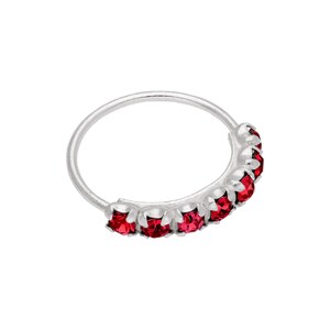 Può includere: Un anello per il naso argentato con una fila di gemme rosse vibranti. L'anello è circolare, con le gemme disposte lungo una sezione curva. Le gemme sono di un rosso intenso, aggiungendo un tocco di colore all'anello d'argento.