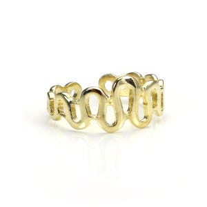 Puede incluir: Un anillo dorado con un diseño continuo y ondulado. El patrón del anillo consiste en formas ovaladas alargadas e interconectadas, creando una estética fluida y calada. El anillo está sobre un fondo blanco, resaltando su superficie pulida.