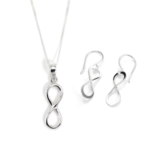 May include: A silver infinity symbol necklace and matching earrings set. The pendant and earrings feature a polished, open-loop design, suspended from a delicate chain and ear wires. The jewellery is displayed against a white background.
