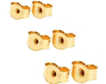 May include: Six gold-coloured earring backs are shown against a white background. The earring backs have a butterfly shape with a central hole for the earring post. The backs are made of a shiny, metallic material.
