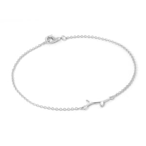 May include: A delicate silver bracelet with a fine chain and a small, stylized branch charm. The bracelet has a lobster clasp closure. The jewellery is designed for everyday wear and adds a touch of nature-inspired elegance.