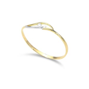 May include: A gold bracelet with a minimalist design. The bracelet has a small, clear gemstone set in a white metal accent. The band is a smooth curve, creating an elegant aesthetic. The jewellery is set against a white background.