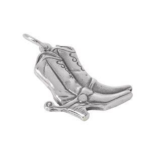 Op de afbeelding: Een zilverkleurige metalen bedel in de vorm van een paar cowboylaarzen. De bedel is voorzien van gedetailleerde stikpatronen op de schachten, een gedefinieerde hak en een kleine spoor aan de achterkant van de hak. Bovenaan zit een klein rond ringetje.