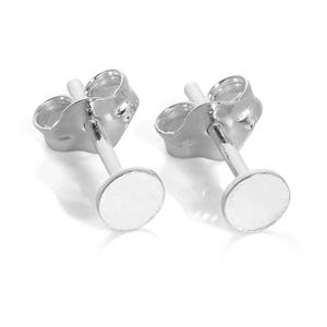 May include: A pair of small, silver-colored stud earrings. Each earring features a circular, flat disc attached to a post with a butterfly backing. The earrings are displayed against a white background.