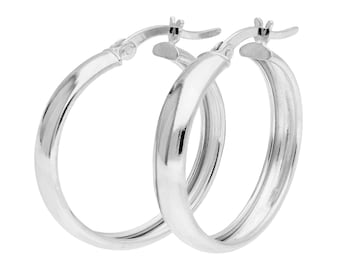 May include: A pair of silver hoop earrings. The earrings have a classic, rounded design with a smooth, polished surface. The hoops are shown against a white background, highlighting their reflective quality.