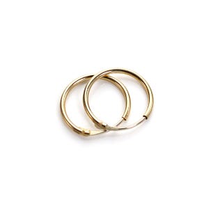 May include: Two gold-colored hoop earrings on a white background. The earrings are circular, with a simple, classic design. The hoops are connected with a silver-colored clasp.