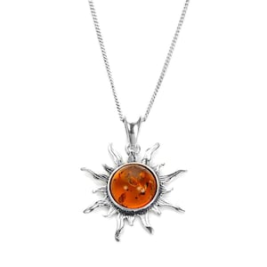 Puede incluir: Un collar de plata con un colgante de sol. El colgante tiene un centro de color ámbar y un diseño de sol. La cadena es de plata fina. La joya se muestra sobre un fondo blanco. El diámetro del colgante es de aproximadamente 2,5 cm.