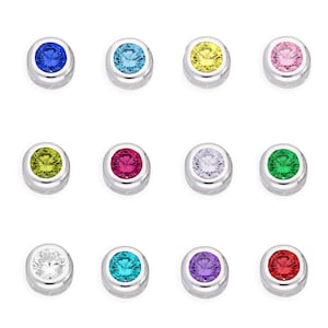 Könnte beinhalten: Eine Sammlung von zwölf kreisförmigen silberfarbenen Metallanhängern, die jeweils mit einem einzelnen runden facettierten Edelstein in verschiedenen Farben wie Blau, Hellblau, Gelb, Pink, Limettengrün, Magenta, Weiß, Smaragdgrün, Türkis, Violett und Rot besetzt sind.