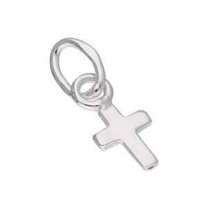Può includere: Un piccolo ciondolo a forma di croce color argento, con un anello nella parte superiore per attaccarlo a una collana o un braccialetto. La croce ha un design semplice e classico con bordi arrotondati.