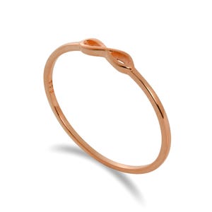 May include: Rose gold infinity ring. The ring has a slender band and an infinity symbol. The ring is made of a shiny, rose-coloured metal. The infinity symbol is a classic and timeless design.