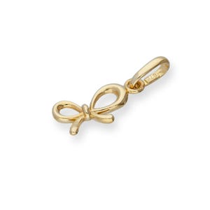 May include: A polished yellow gold pendant shaped like a small bow. The charm features a smooth, reflective surface and includes a small, integrated jump ring at the top for attachment to a chain. The metal is stamped with the number 375.