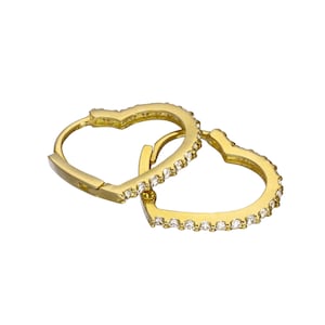 May include: A pair of gold-colored heart-shaped hoop earrings. Each earring is lined with small, clear gemstones. The earrings are shown against a white background, with one earring partially open to show the clasp.