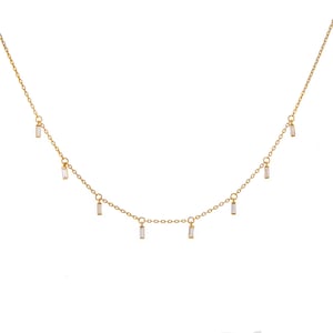 May include: A delicate gold-colored necklace with small, rectangular, clear gemstones dangling from the chain. The necklace has a simple design, with the gemstones evenly spaced along the chain.
