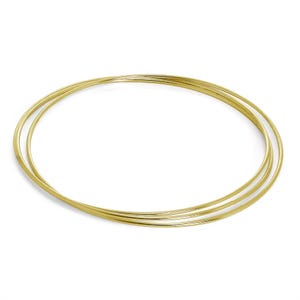 Op de afbeelding: Drie goudkleurige armbanden, elk een dunne, gladde band, zijn in een geneste configuratie gerangschikt. De armbanden staan tegen een witte achtergrond, wat een eenvoudige, elegante presentatie creëert. De sieraden zijn waarschijnlijk voor de pols.