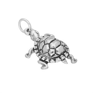 May include: A silver-toned metal turtle charm featuring a detailed, textured shell with a segmented pattern and four extended flippers. The charm includes a small circular jump ring attached to the head, designed for easy attachment to jewellery.