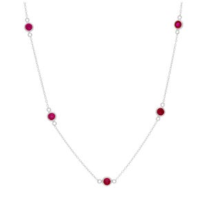 May include: A delicate silver necklace featuring five round, vibrant red gemstones evenly spaced along the chain. The gemstones are set in a simple bezel setting, creating a minimalist and elegant design. The necklace is displayed against a plain white background.