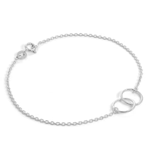 May include: A delicate silver bracelet featuring a chain and two interlocking circles. The bracelet has a lobster clasp closure. The jewellery is displayed on a white background, highlighting its minimalist design and reflective surface.